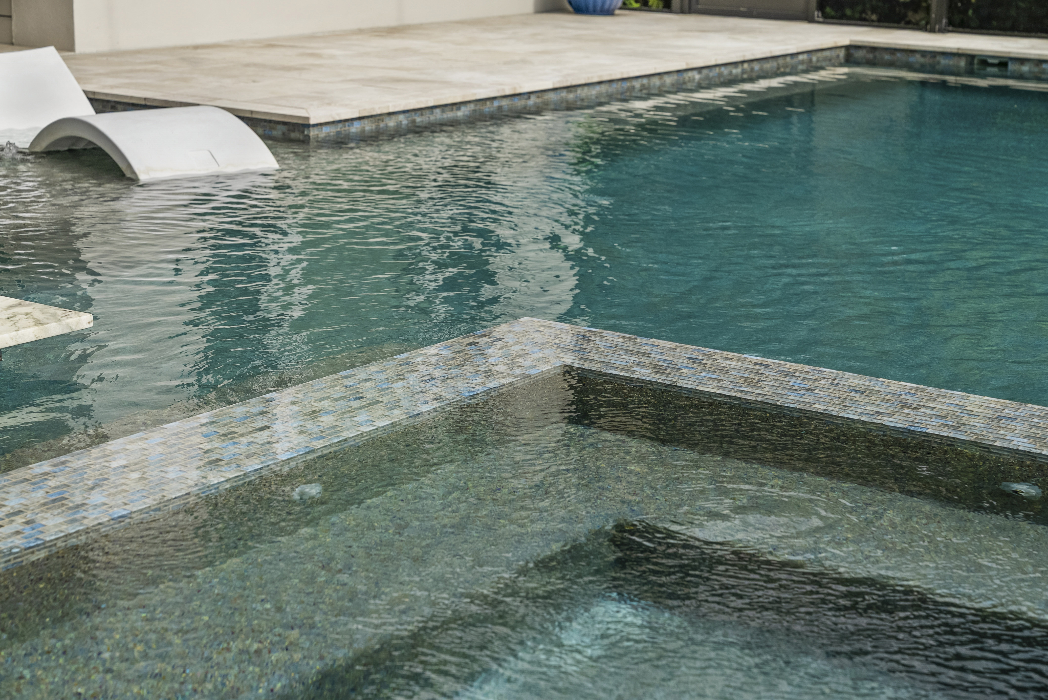 Spillover spa with water cascading into pool below, warm LED lighting at dusk